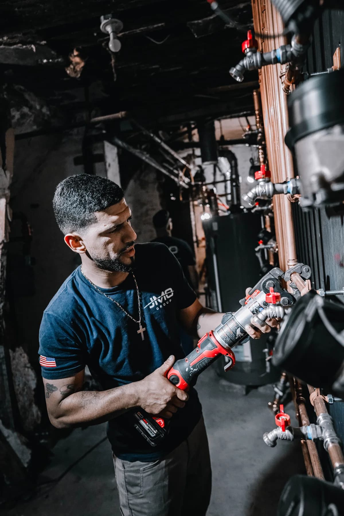 JMO technician using a press tool on copper pipework in a mechanical room